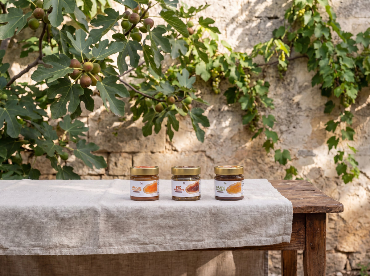 Three preserve jars on a linen-draped table beneath a fig tree in Puglia